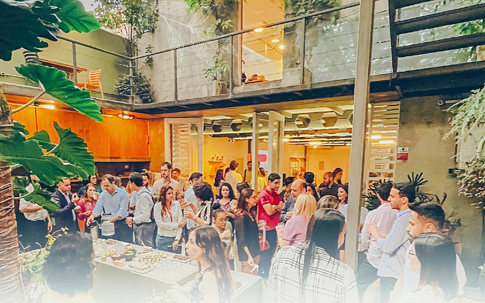Evento corporativo no pátio interno do Espaço aFlora, com vegetação, mesa de catering e convidados em networking