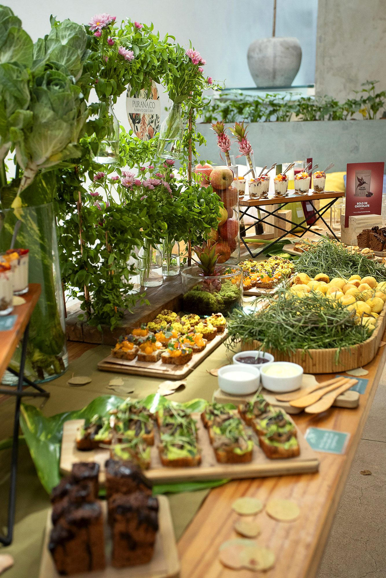 Mesa completa do catering Purana com flores, ervas frescas, torradas e bolos
